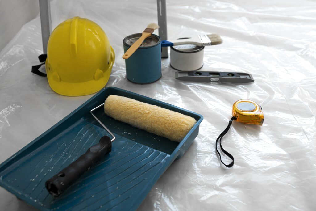 Home renovation tools including paint rollers, safety helmet, and measuring tape on a wooden floor – representing interior upgrade planning.