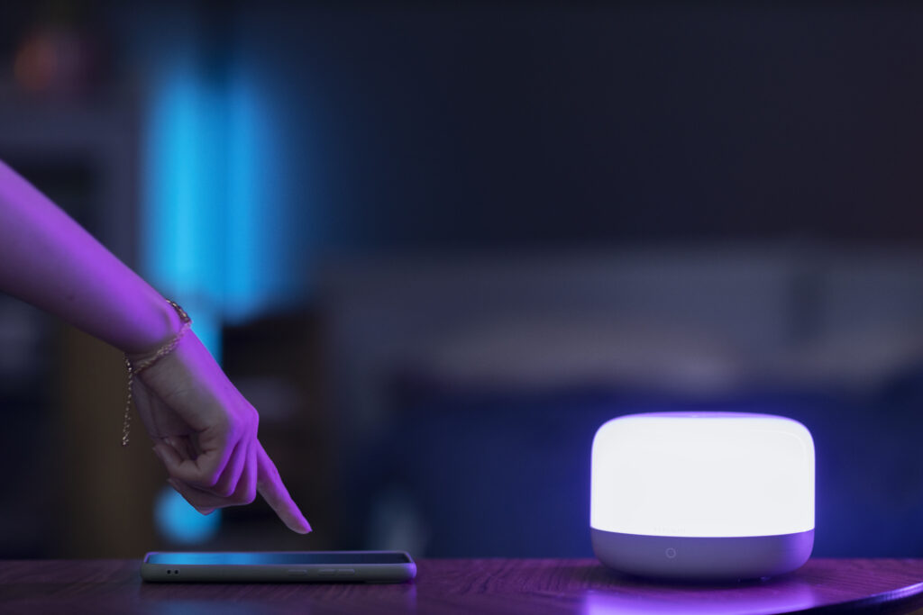 Person controlling smart home lighting with smartphone app in modern living room, ambient light setup