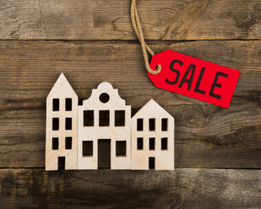 Wooden house model with red SALE tag on rustic background – symbol of quick property sale