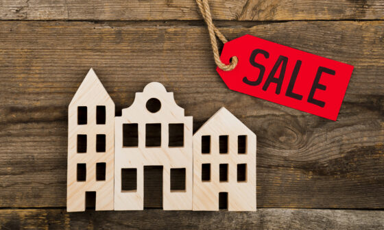 Wooden house model with red SALE tag on rustic background – symbol of quick property sale
