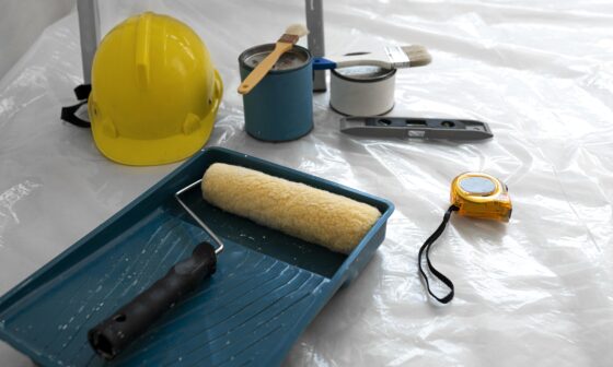 Home renovation tools including paint rollers, safety helmet, and measuring tape on a wooden floor – representing interior upgrade planning.