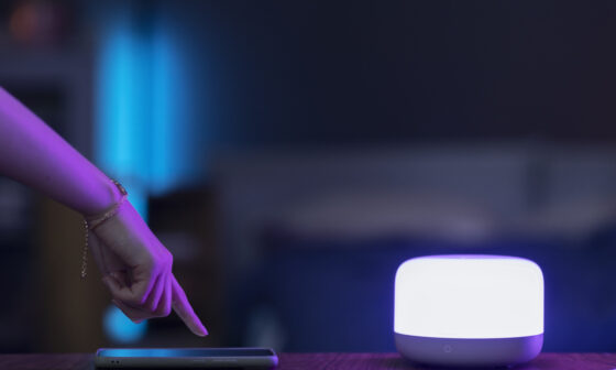 Person controlling smart home lighting with smartphone app in modern living room, ambient light setup