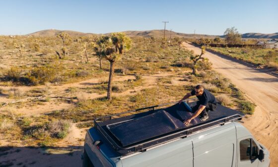 Person installing a 200W flexible solar panel on the roof of a camper van in a sunny desert landscape.